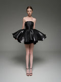 A model wearing a black strapless mini dress with a flared, tiered skirt, standing against a dark gray studio background. The brand name 'Lusilk' is displayed at the top of the image.