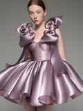 A model wearing a lavender satin mini dress with oversized bow details on the shoulders and a flared skirt, photographed against a solid gray studio background.