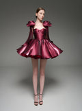 A model wearing a metallic magenta formal dress with dramatic shoulder details and a flared skirt, standing against a dark gray studio background. The brand name 'Lusilk' is displayed at the top.