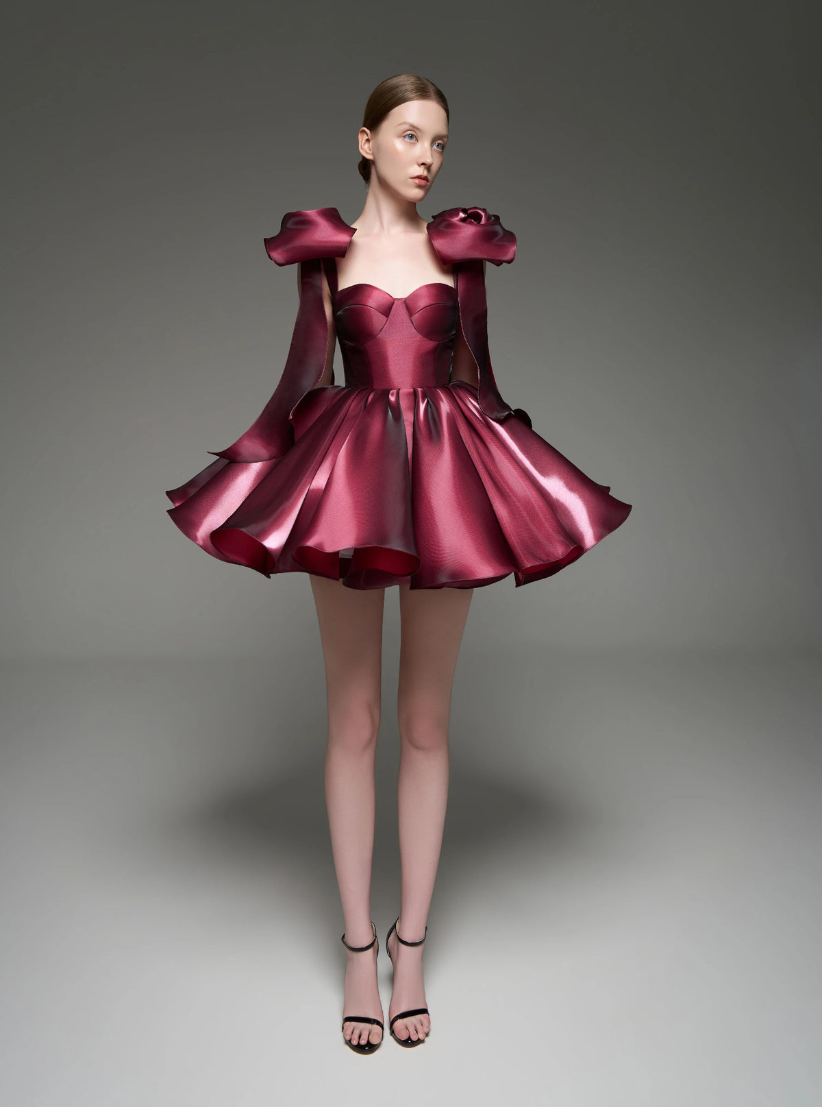 A model wearing a metallic magenta formal dress with dramatic shoulder details and a flared skirt, standing against a dark gray studio background. The brand name 'Lusilk' is displayed at the top.